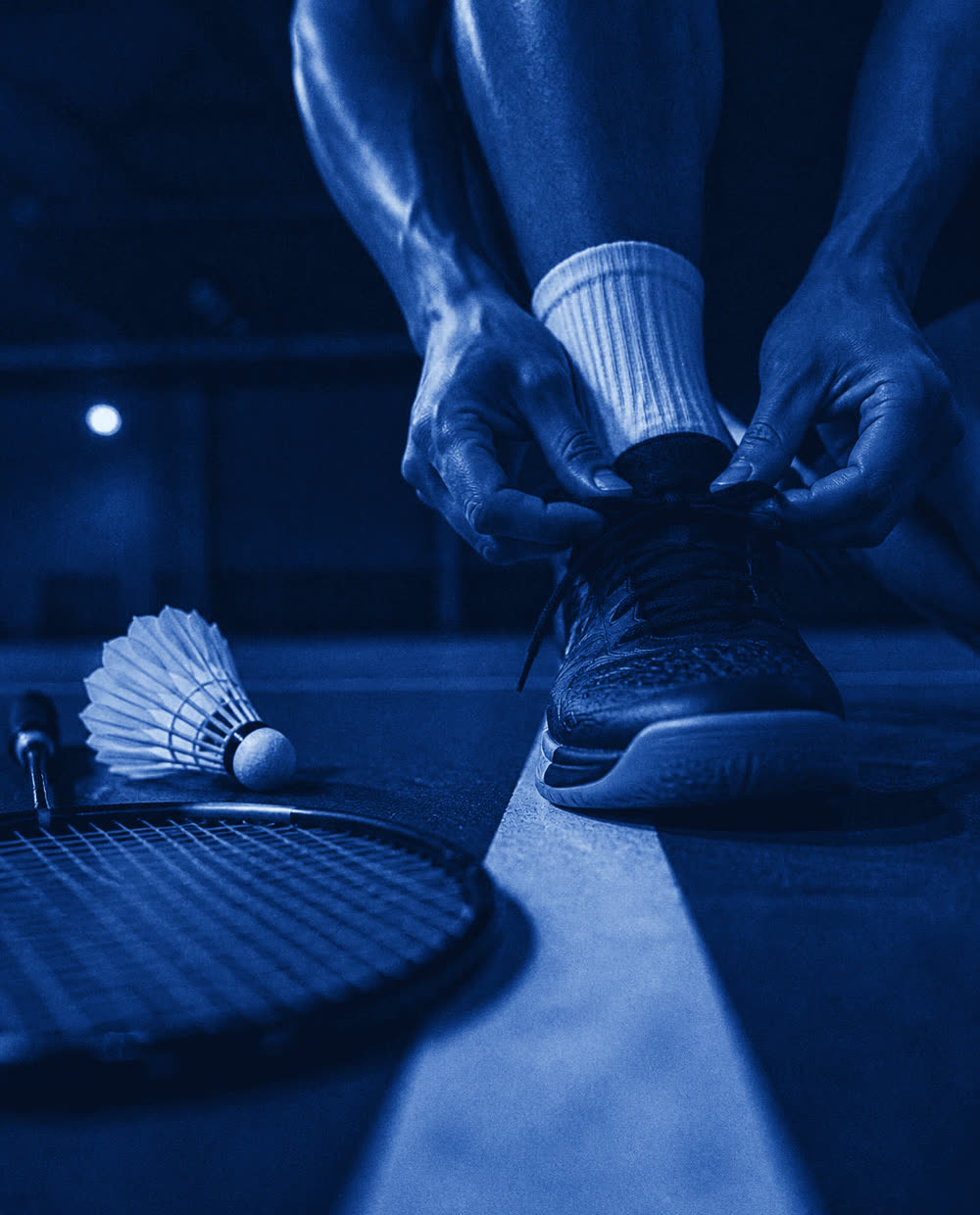 A player lacing court shoes beside a racket and shuttle